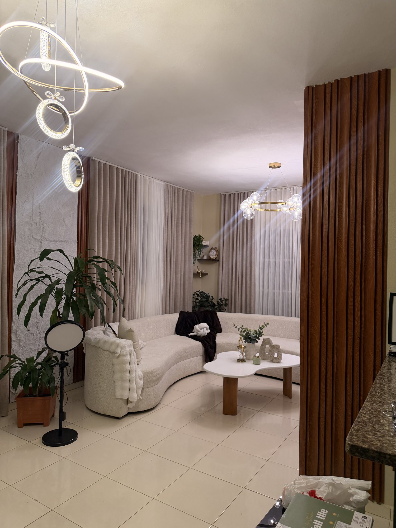Sala con sofá curvo blanco, columna de listones de madera y lámpara de anillos de luz
